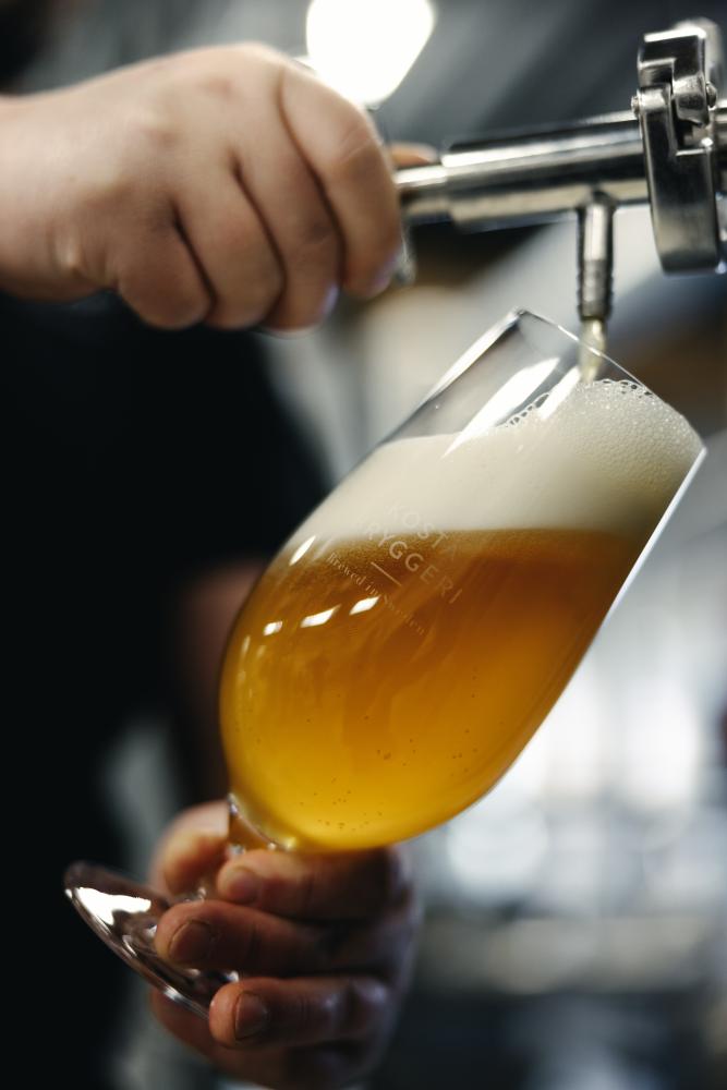 Händer häller upp öl i glas från tank