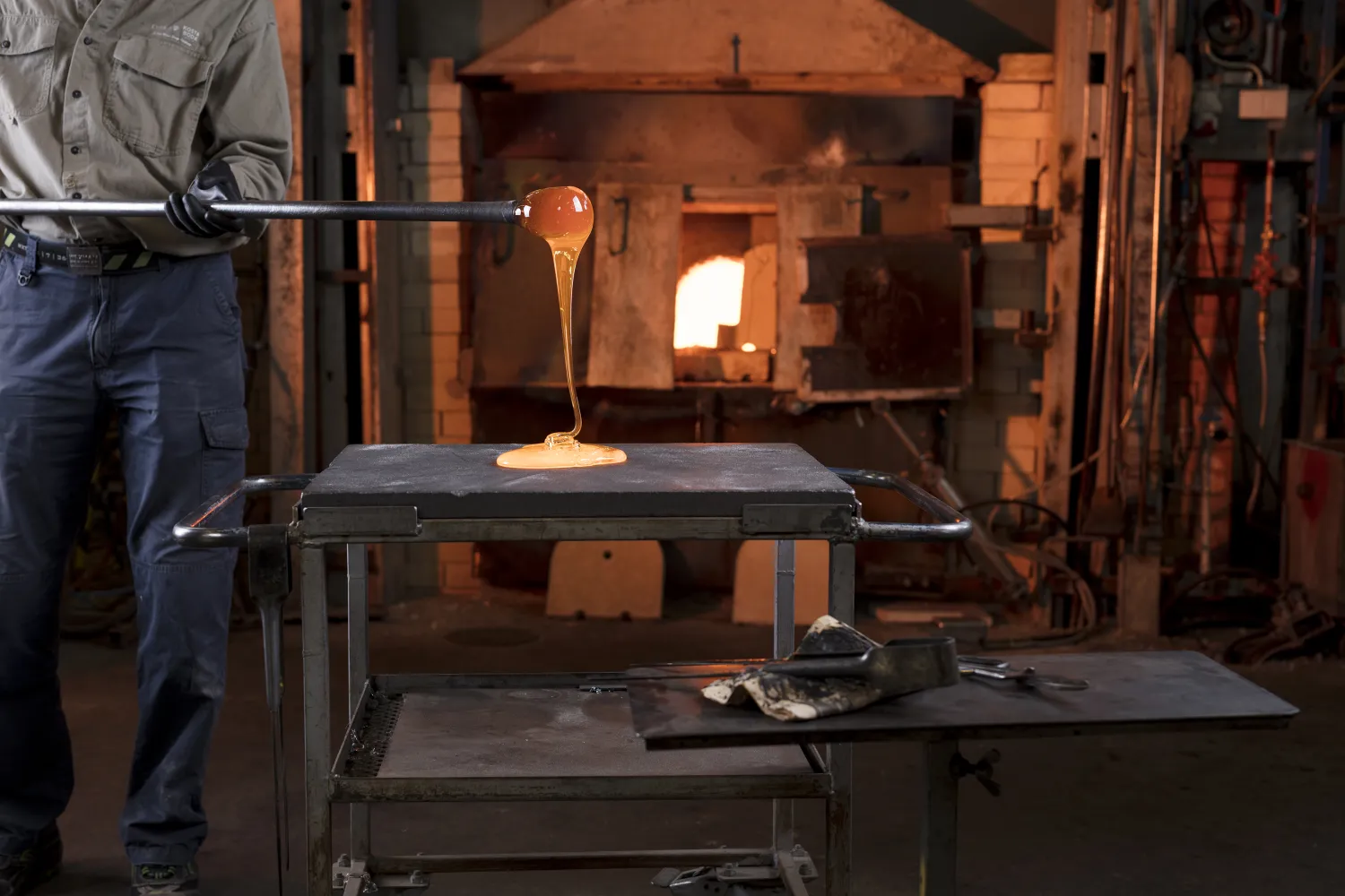 Glasblåsare med glödande glas framför glasugn