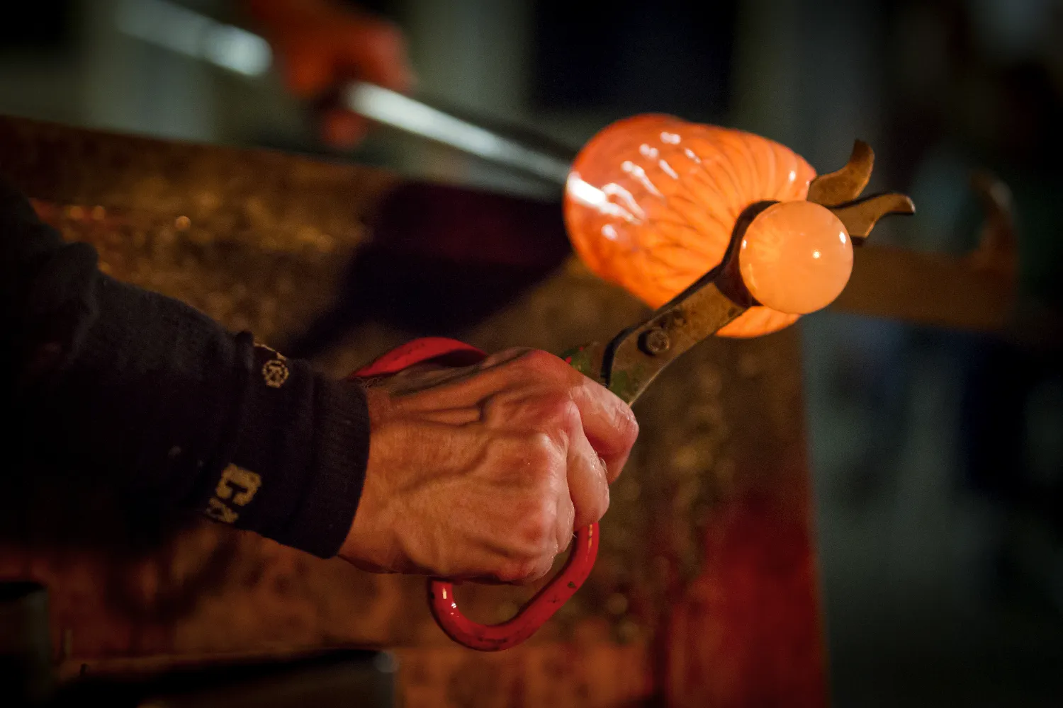 Närbild på glasblåsare hanterar det heta orangefärgade glaset